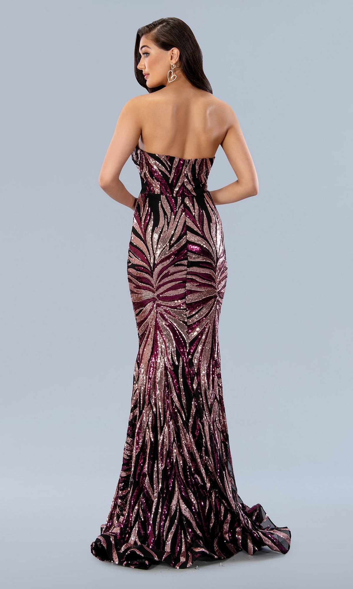 A woman wears the Long Prom Dress 24134 by Stella Couture—a floor-length strapless mermaid dress with pink and black geometric sequins—standing against a plain light gray background.